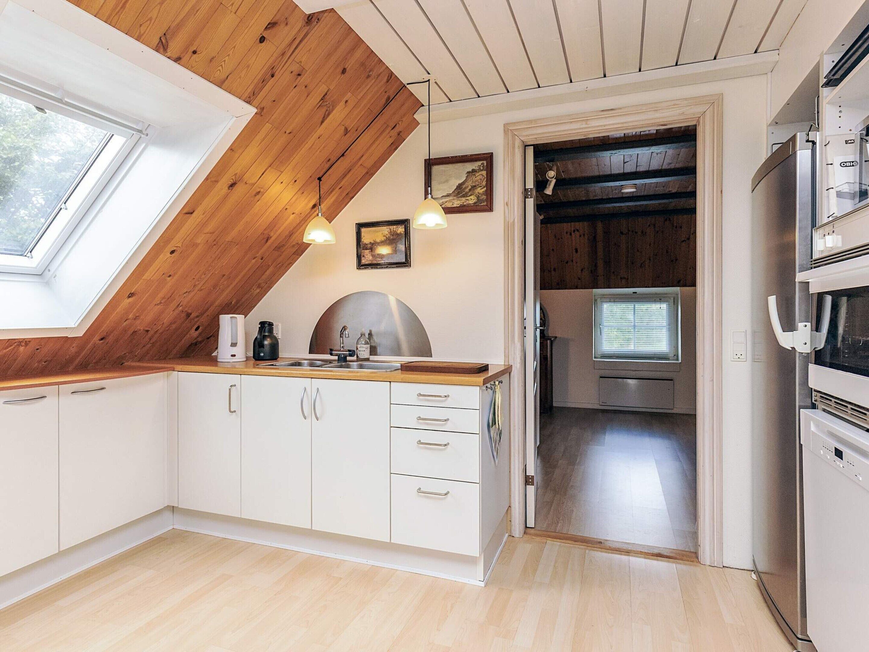 A modern kitchen with white cabinets, a wooden ceiling, and a skylight.