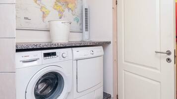 Een kleine wasruimte met een Bosch wasmachine, een emmer en een wereldkaart aan de muur.