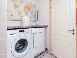 A compact laundry area with a Bosch washing machine, a small bucket, and a world map on the wall.