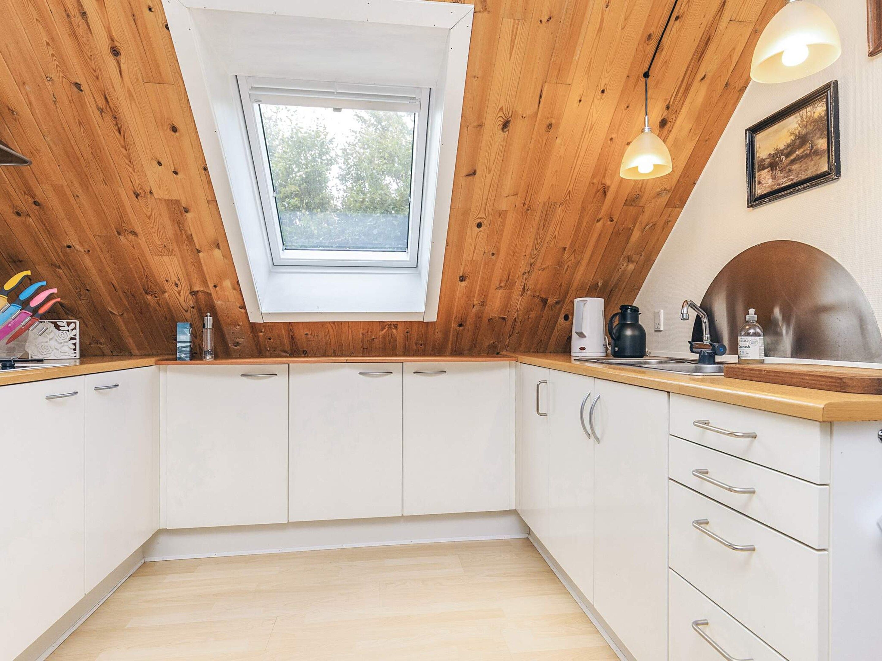 A kitchen with white cabinets, a wooden ceiling, a skylight, and a wooden countertop.