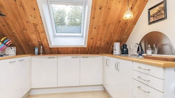 A kitchen with white cabinets, a wooden ceiling, a skylight, and a wooden countertop.