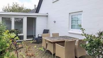 Een terras met een tafel en stoelen, een schuifpui en een wit gevelpand.