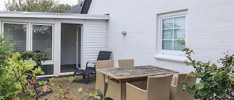 A patio with a table and chairs, a sliding glass door, and a white house exterior.