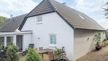 A white house with a tiled roof, a patio with a table and chairs, and potted plants.