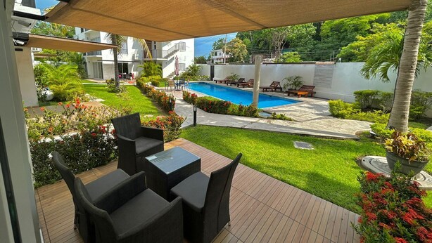 An outdoor patio with a pool, surrounded by greenery and a covered seating area.