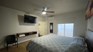 A bedroom with a bed, a ceiling fan, a TV, a window, and a door.