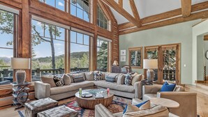 A spacious living room with large windows, a sectional sofa, and a coffee table. - Luxury Ski-in/out Retreat | Timber Haven (Avon)