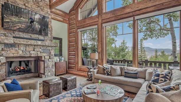 A spacious living room with a stone fireplace, large windows, and a cozy seating area. - Luxury Ski-in/out Retreat | Timber Haven (Avon)