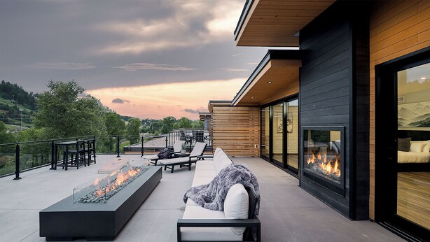 Une terrasse extérieure moderne, dotée d’un foyer, de sièges et offrant une vue sur le paysage.