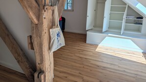 Ein Zimmer mit freiliegenden Holzbalken, einem weißen Schrank mit geöffneten Türen und einer weißen Tasche, die an einem Balken hängt.