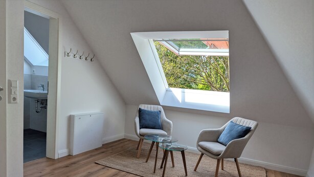 Ein Zimmer mit schrägem Dach, einem Oberlicht, zwei Sesseln, einem Glastisch und Blick ins Grüne.