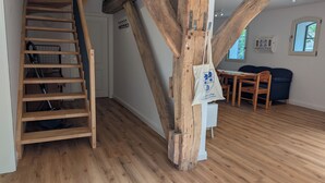 Eine Holztreppe, ein Essbereich mit Tisch und Stühlen sowie ein Holzbalkenbau.