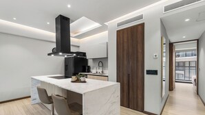 Una cocina moderna con una isla de mármol, dos taburetes de bar, una campana extractora negra y una puerta de madera.