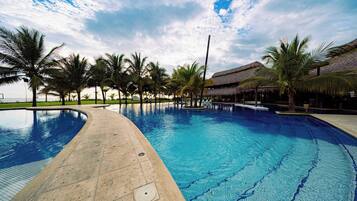 A large outdoor swimming pool with palm trees and a thatched-roof structure.