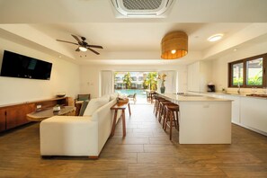 A modern living room with a sofa, a TV, a ceiling fan, and a view of a pool. - Private jacuzzi and balcony in 2-Br villa (Monterrico)