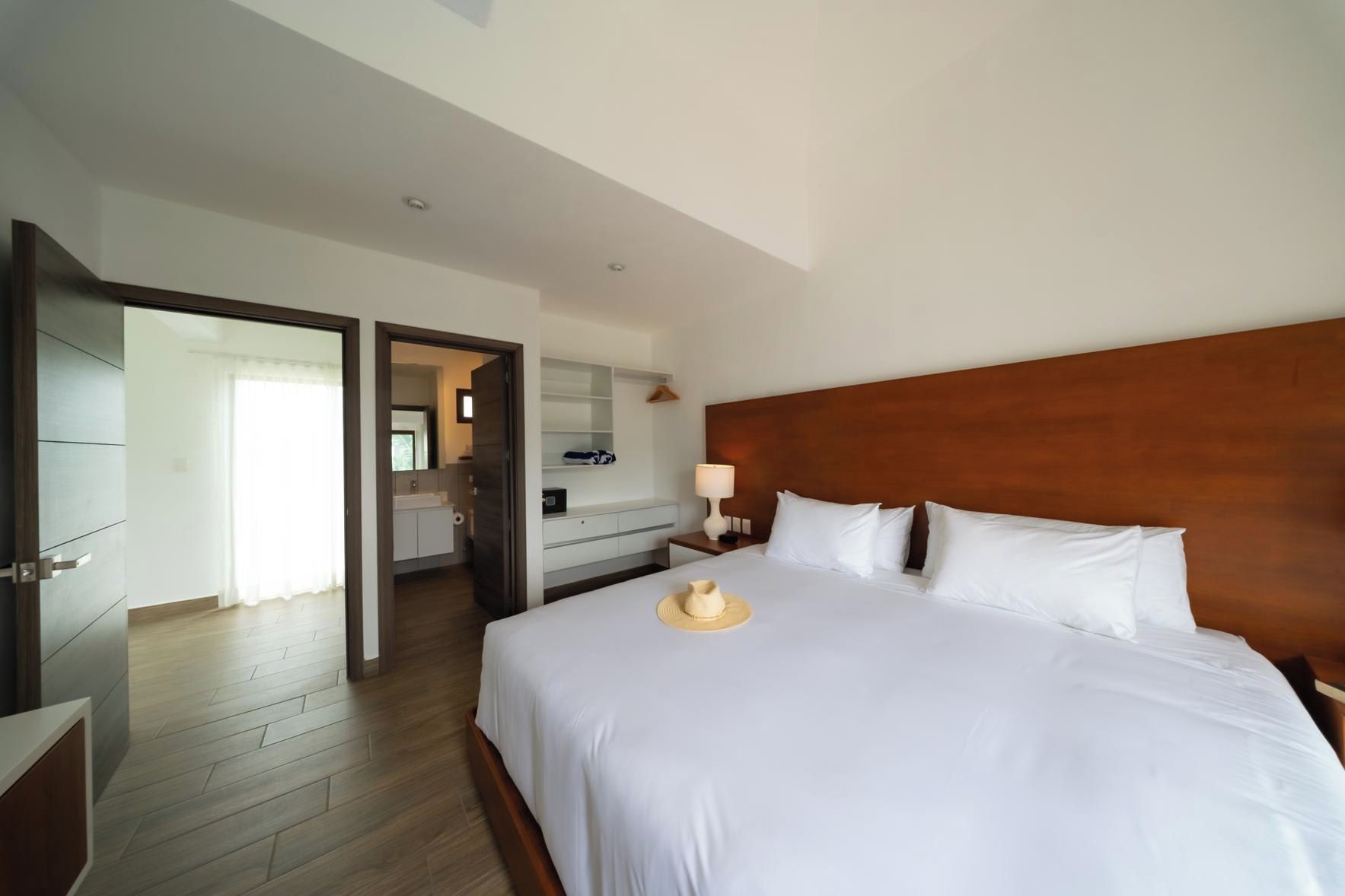 A hotel room with a large bed, a wooden headboard, a nightstand with a lamp, and a bathroom visible through an open door.