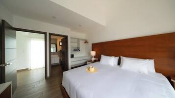 A hotel room with a large bed, a wooden headboard, a nightstand with a lamp, and a bathroom visible through an open door.