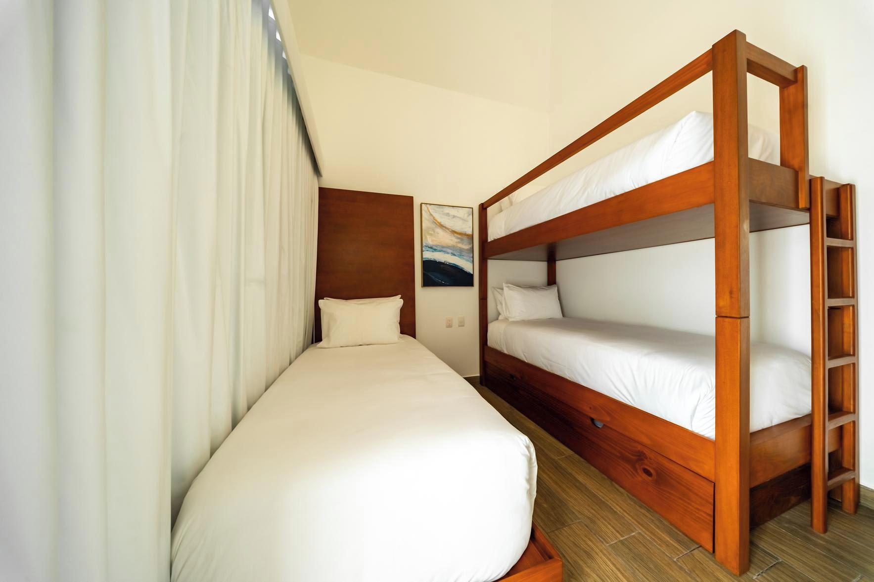 Ett hotellrum med en våningssäng, en enkelsäng, en sänggavel i trä och en tavla på väggen.