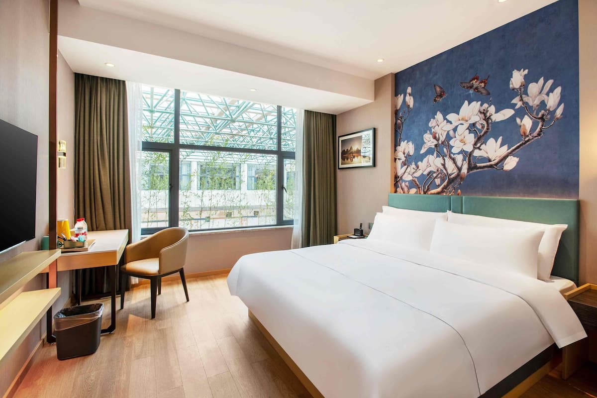 Une chambre d’hôtel avec un grand lit, un bureau avec une chaise, une tél évision et une fenêtre avec des rideaux.