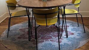 Une table ronde en bois, sur laquelle est posé un vase rempli de fleurs oranges, entourée de chaises jaunes, le tout sur un tapis à motifs.