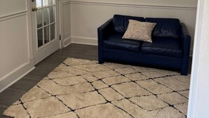Une pièce avec un canapé bleu foncé, un tapis blanc et une fenêtre donnant sur un beau paysage.