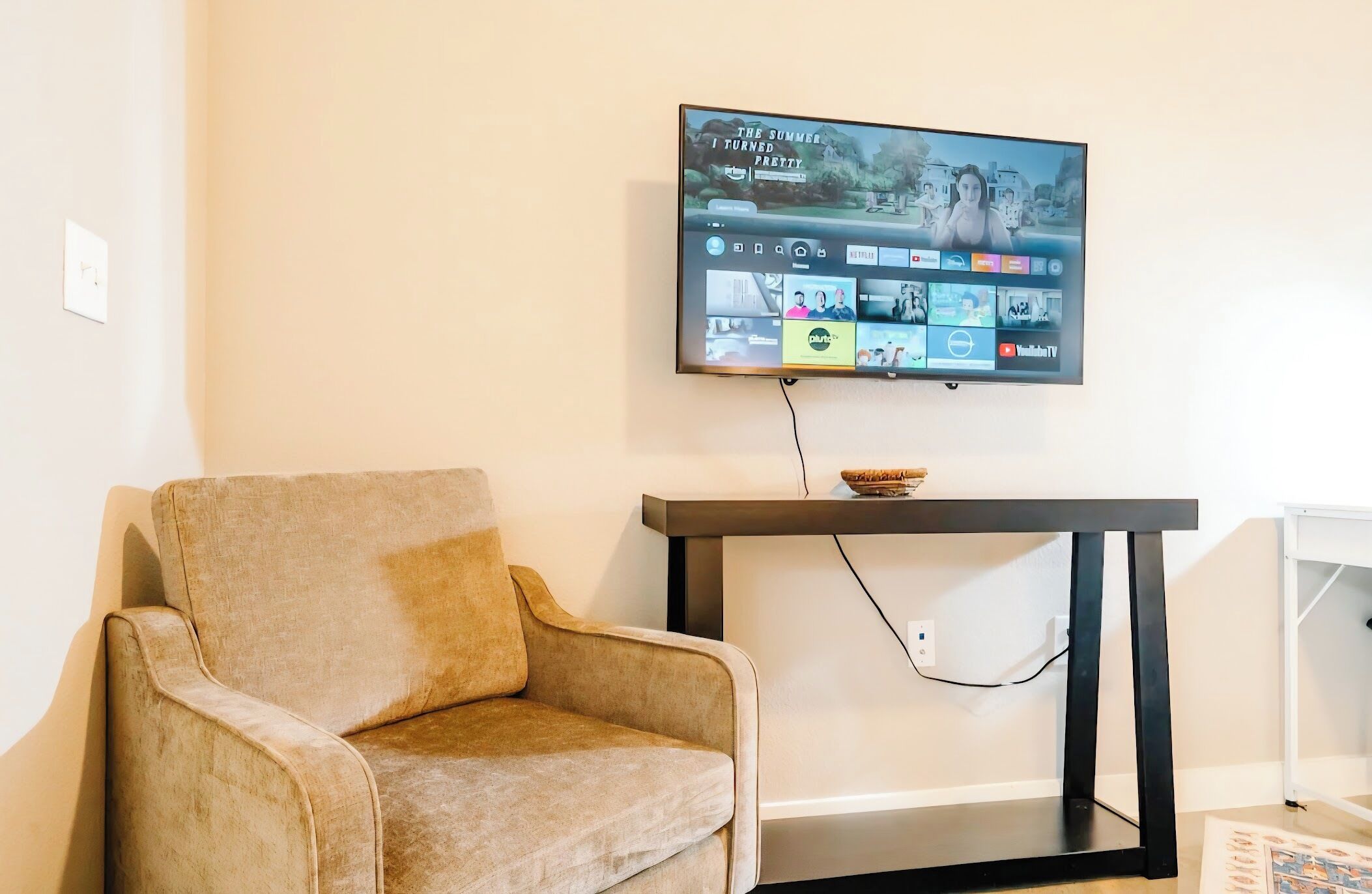 A living room with a beige armchair, a black TV on a stand, and a white shelf.