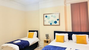 Une chambre d’hôtel avec deux lits, chacun recouvert d’une couverture bleue et agrémenté d’oreillers blancs, un tableau au mur et un lustre.