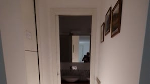 A narrow hallway with a wooden floor leading to a bathroom with a sink and mirror.
