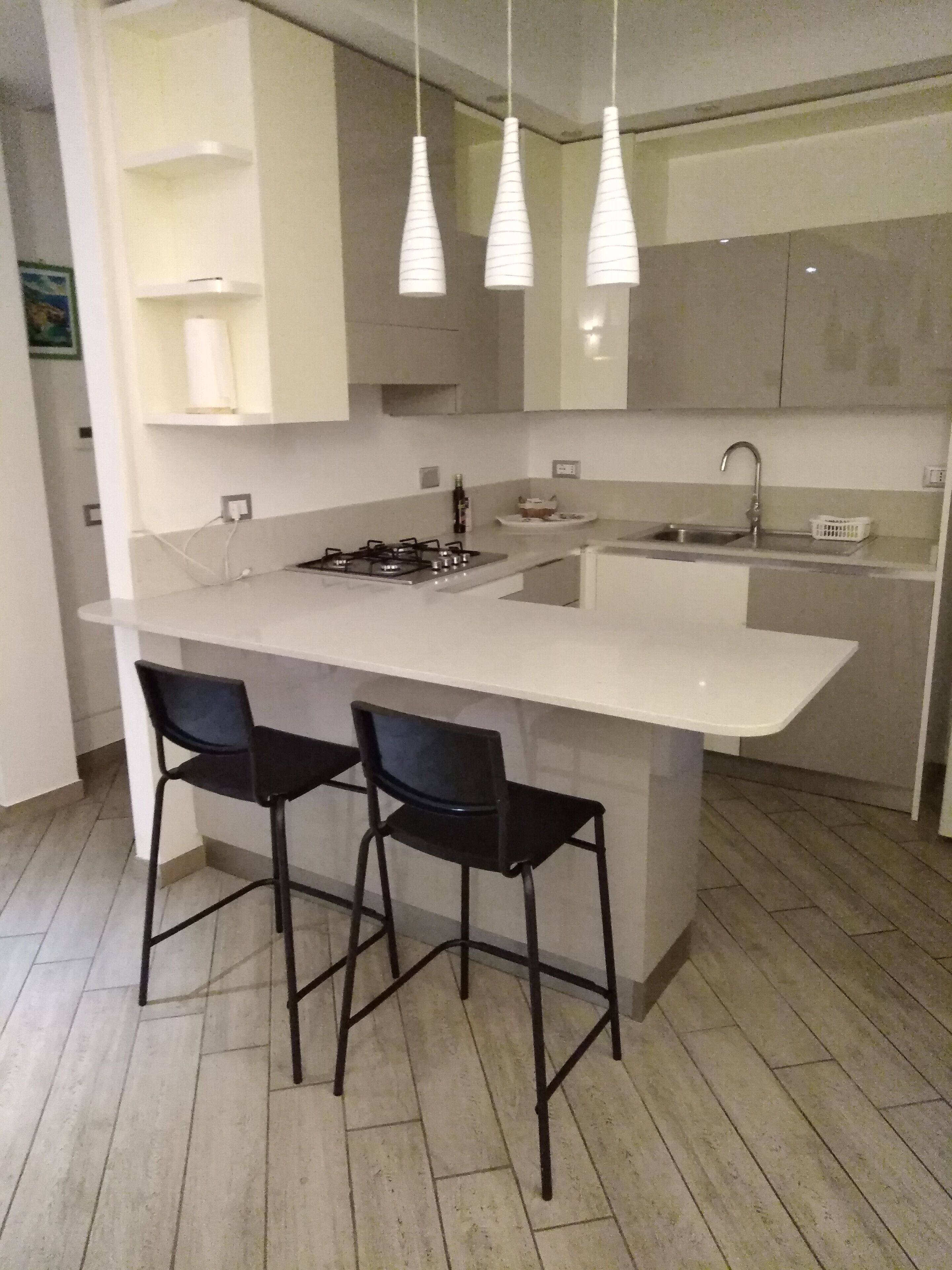 A modern kitchen with a central island, two black bar stools, a gas stove, a sink, and pendant lights.