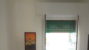 A room with a wooden crib, a bed, a framed picture on the wall, and a door leading outside.