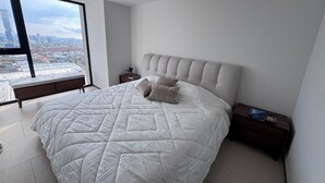 A modern bedroom with a large bed, a view of a cityscape through a large window, and a city view from the window.