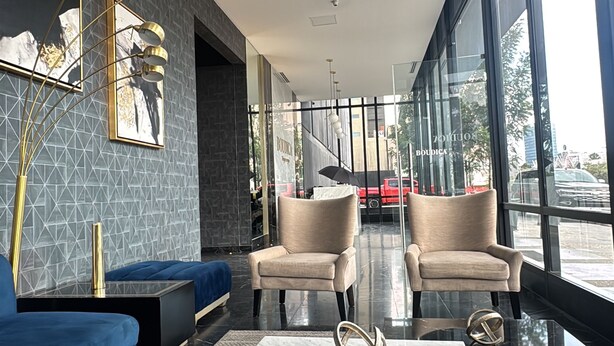 A modern lounge area with a blue sofa, two armchairs, a marble coffee table, and a large window offering a view of the street.