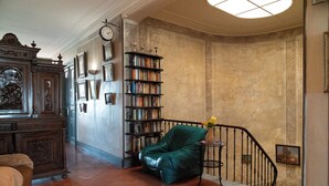 A spacious room with a green leather armchair, a wooden cabinet with artwork, and a bookshelf filled with books.