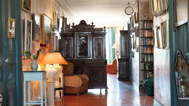 A hallway with a wooden floor, a large ornate cabinet, a bookshelf, and a clock on the wall.