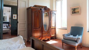 A room with a bed, a wooden wardrobe, a blue armchair, and a painting on the wall.