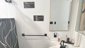 Un bany amb cortina de banyera de disseny blanc i negre, un lavabo blanc amb aixeta negra, un mirall sobre el lavabo i un suport de tovalloles amb una tovallola blanca.