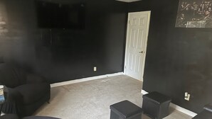 Una habitació amb parets negres, una porta blanca, un televisor de pantalla plana muntat a la paret i una catifes gris.