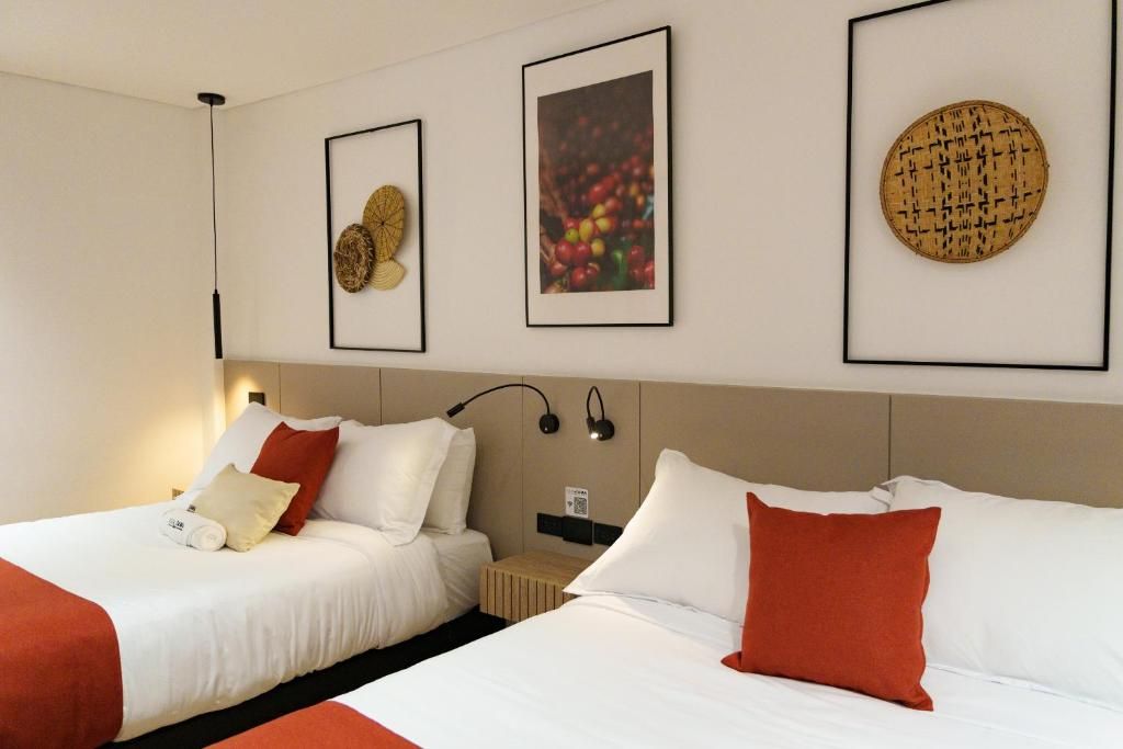 A hotel room with two beds, a wall-mounted lamp, and framed artwork.