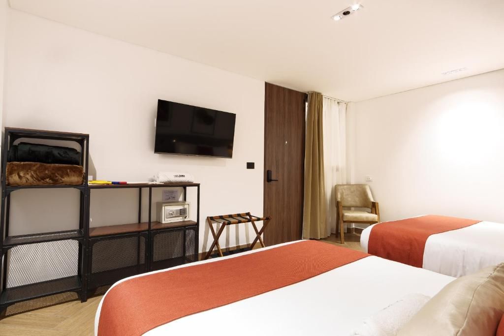 A hotel room with a bed, a TV, a desk with a computer, a chair, and a wardrobe.