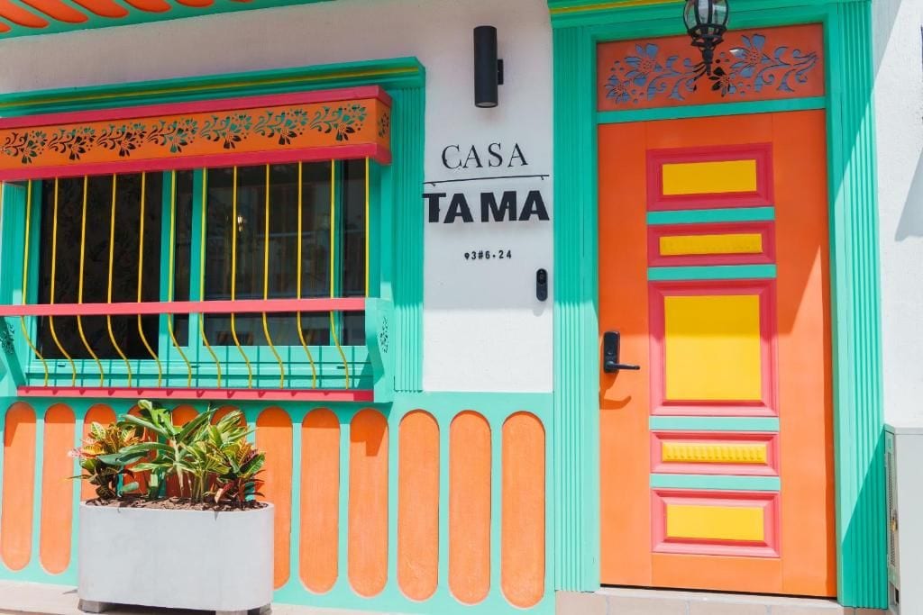 Ein Gebäude mit farbenfroher Fassade, einem Schild mit der Aufschrift 'CASA TAMAL' und einem Blumentopf im Vorbereich.
