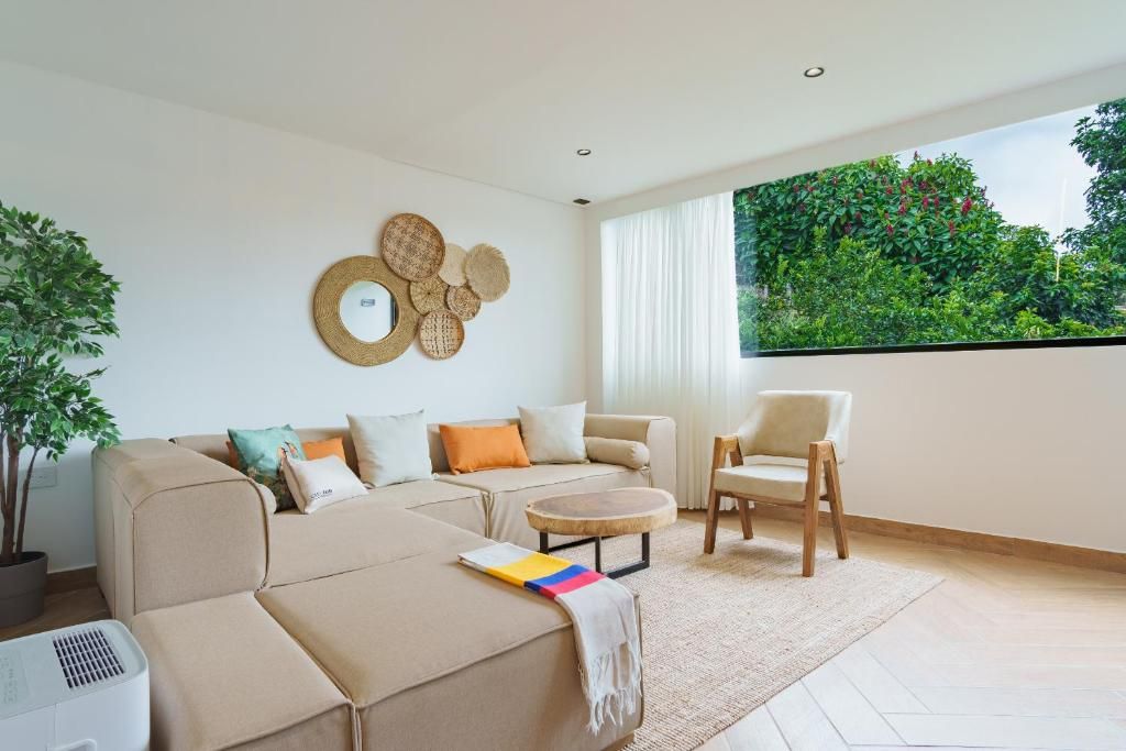 A modern living room with a sofa, a coffee table, and a chair. There is a large window with a view of greenery outside.