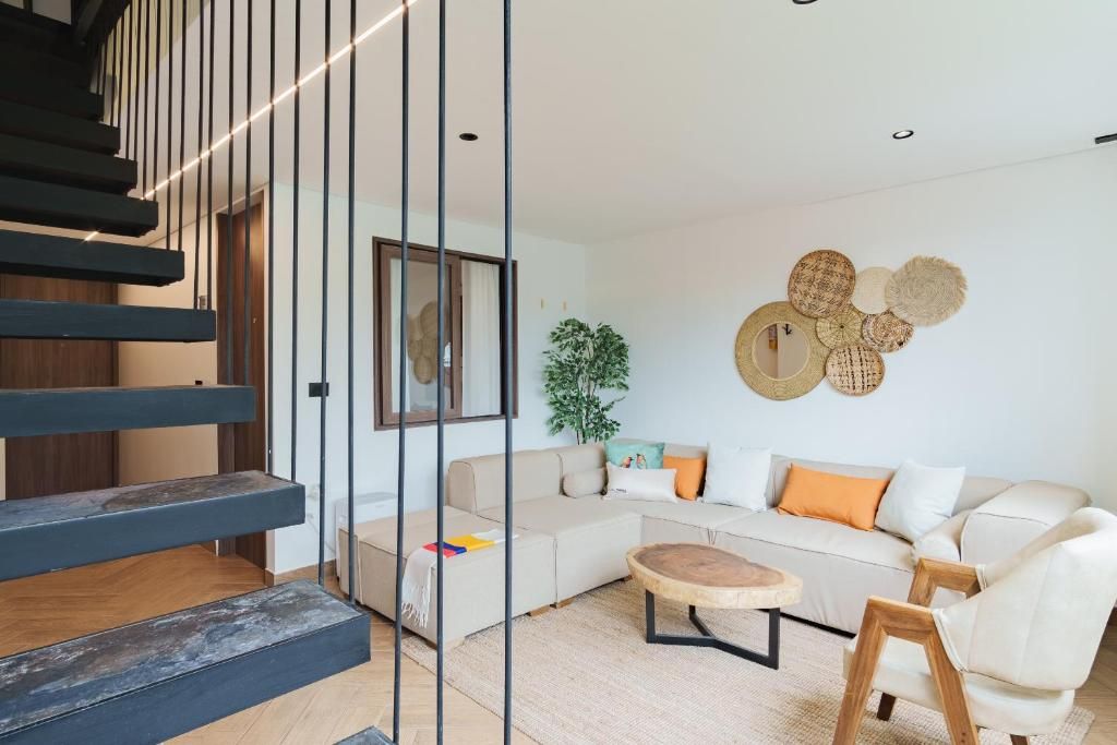 Una sala de estar moderna con una escalera, un sofá modular, una mesa de centro redonda y adornos en la pared.