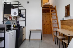 A compact kitchen with a microwave, refrigerator, and shelves. A wooden ladder and a small table are also visible.