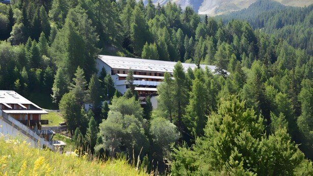 A building surrounded by dense forest with a mountainous backdrop. - Studio Apartment 'Il Nido Di Montagna' (Gressan)