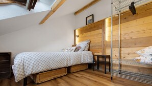 A bedroom with a wooden headboard, a bed with patterned bedding, a small bench, and a metal shelf unit. - Studio Apartment 'Il Nido Di Montagna' (Gressan)