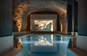 An indoor swimming pool with a natural rock wall and a large window.