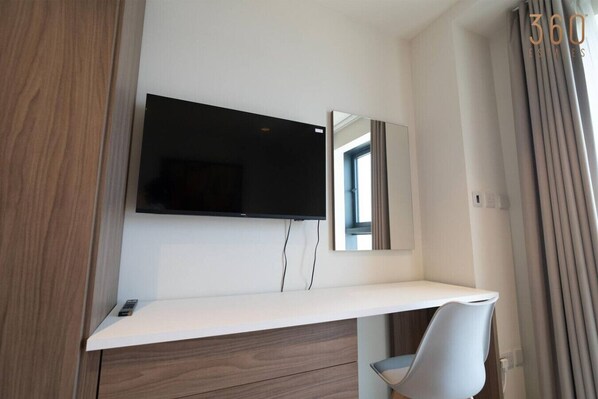 Una habitación de hotel moderna con una televisión de pantalla plana montada en la pared, un escritorio blanco y una silla.