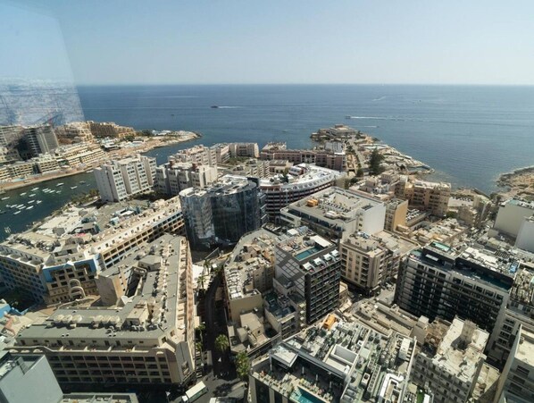 A coastal cityscape with a mix of modern and traditional buildings, a marina with boats, and a clear view of the sea.