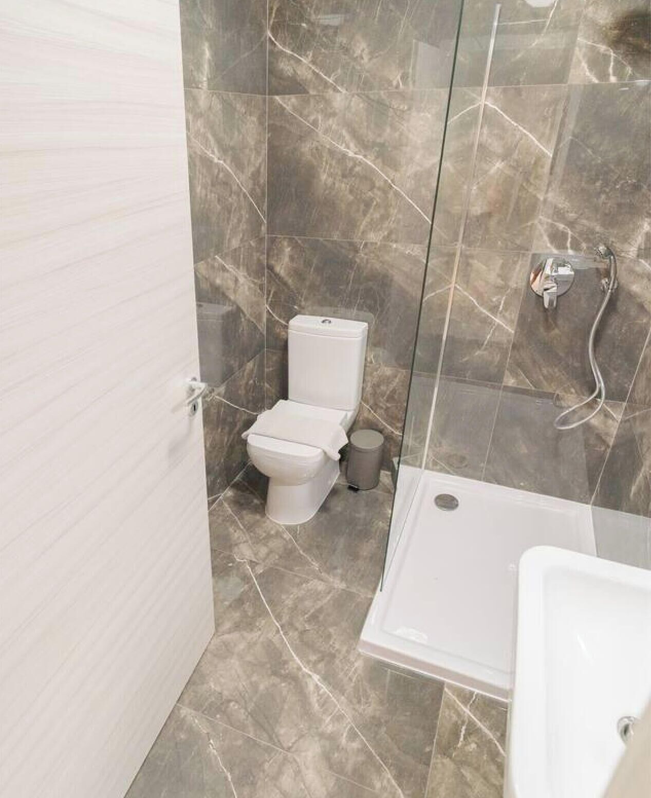 Une salle de bain moderne équipée de toilettes, d’une douche et d’un lavabo, avec des murs en marbre et une paroi de douche en verre.