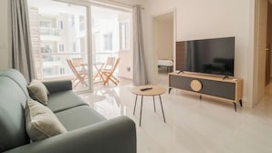 A modern living room with a sofa, a TV on a wooden stand, and a balcony with wooden chairs. - Lovely, fully equipped 2BR home 5 min from beach (St. Paul`s Bay)